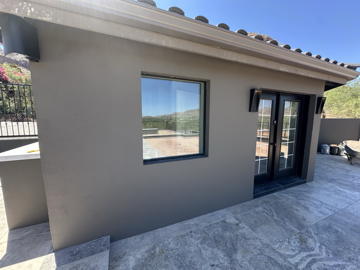Warm-grey smooth stucco patio wall with black window frames and desert mountains beyond