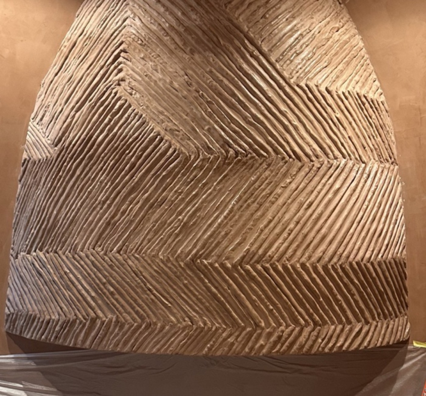 Hand-carved combed chevron relief in terracotta Moroccan clay over a burnished wall