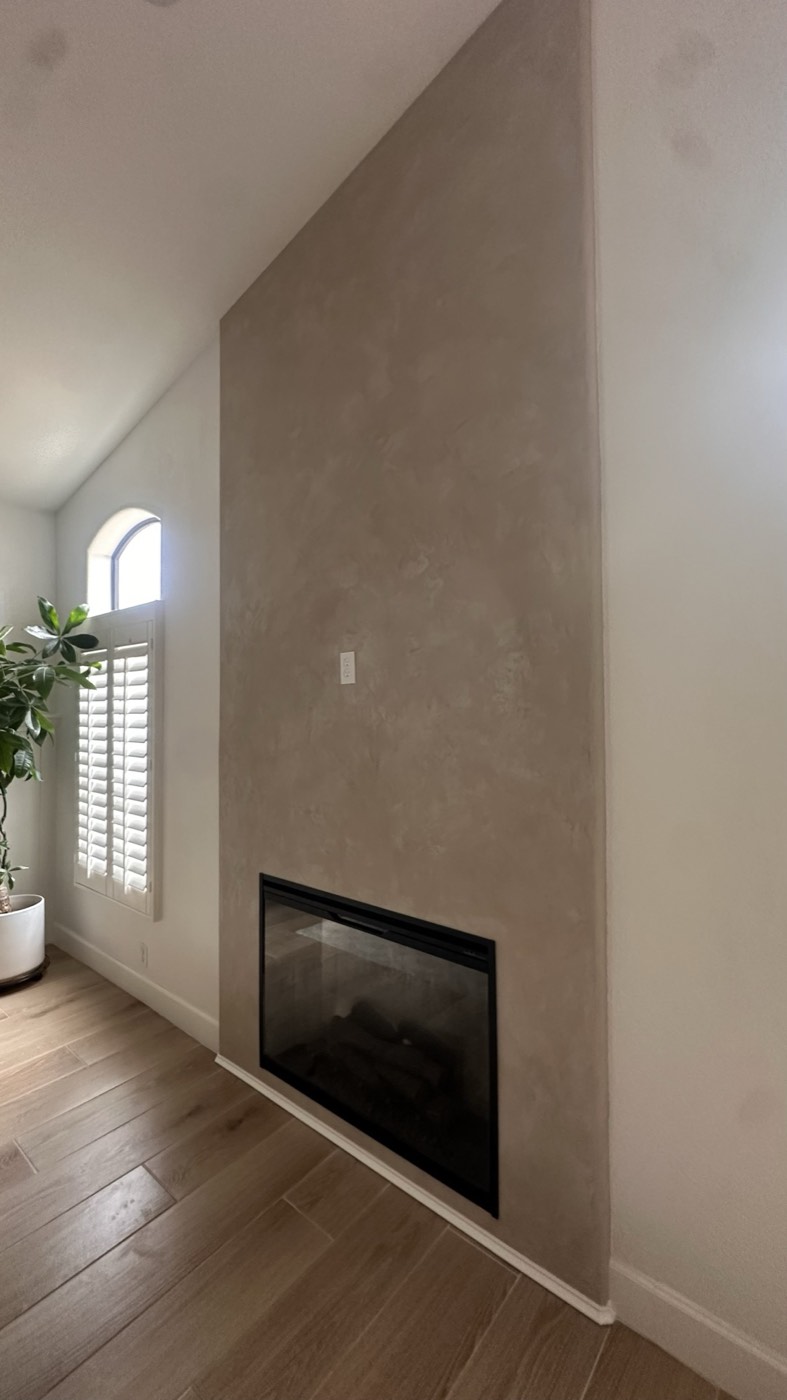 Full-height taupe Roman clay fireplace wall beside an arched shuttered window, Phoenix